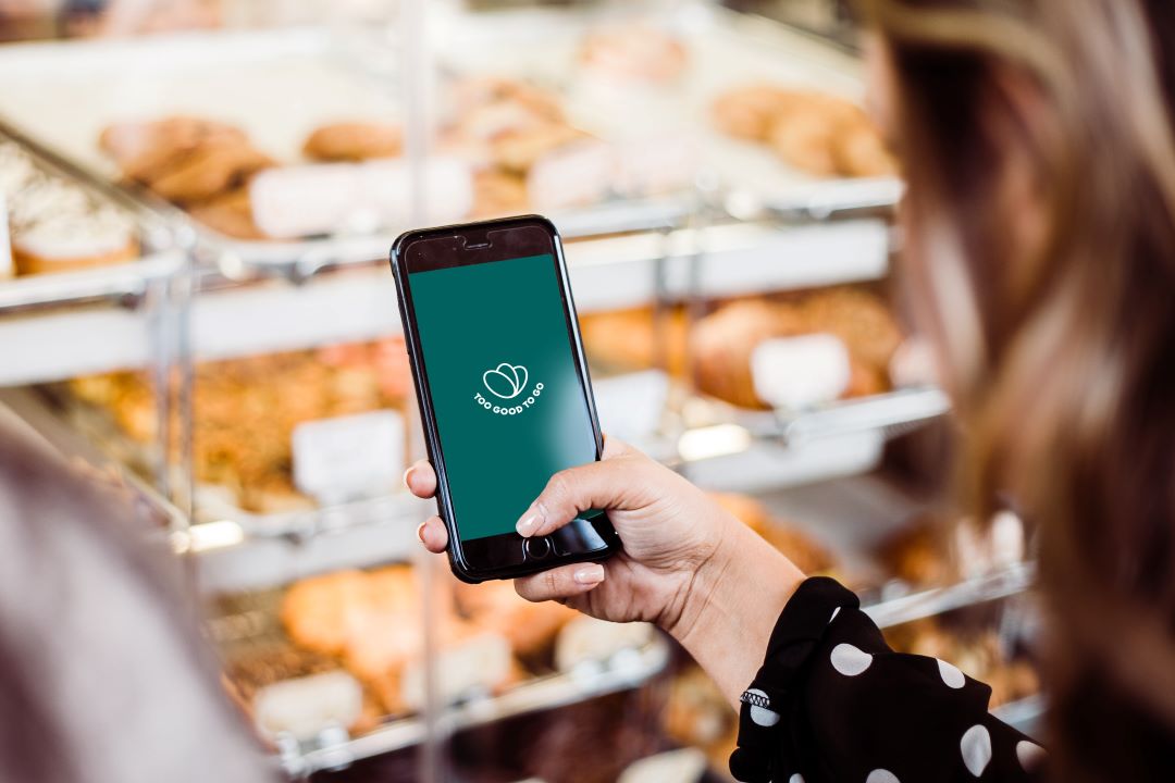 Beim Bäcker wird die Too Good To Go App auf einem refurbed Smartphone geöffnet