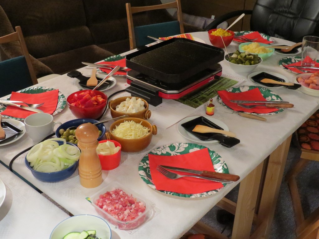 Tisch mit Raclette Grill und Zutaten.